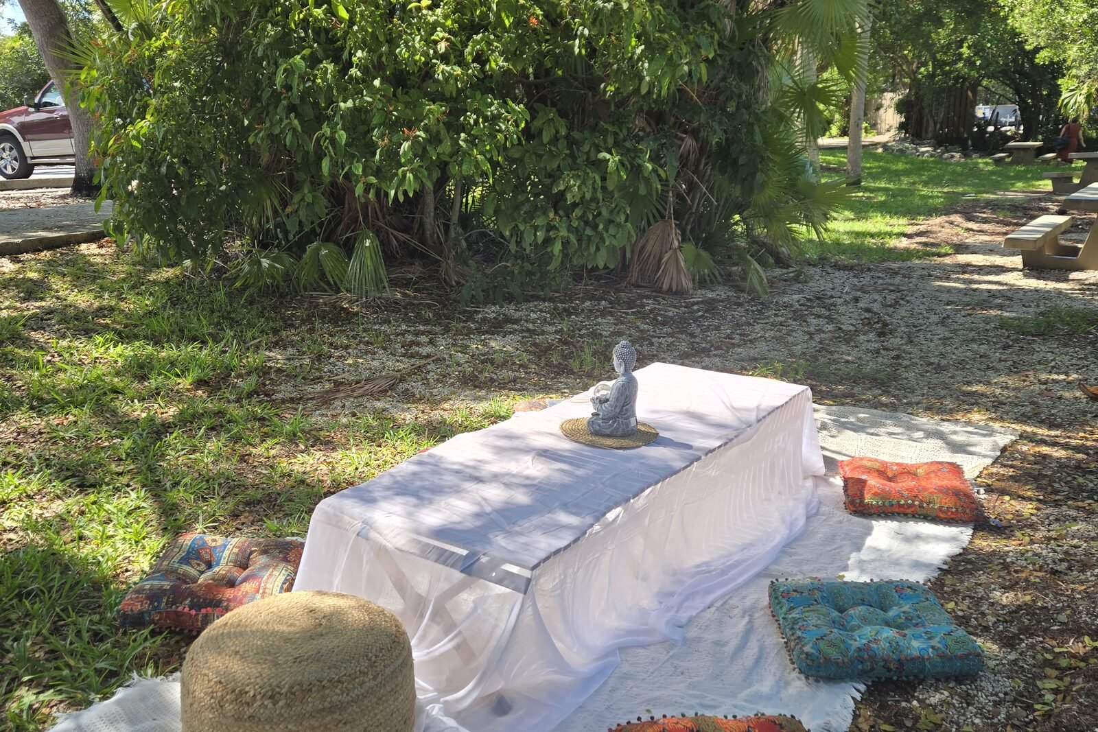 A draped massage table under trees, with cushions and a rug arranged around it.