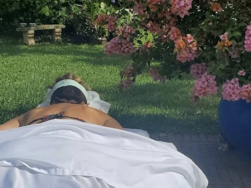 A client face down on Lisa's table in a garden, under flowering bougainvillea