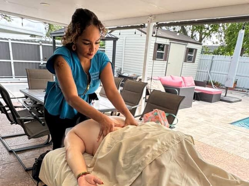 Lisa massaging a client on her table on a covered patio beside a pool